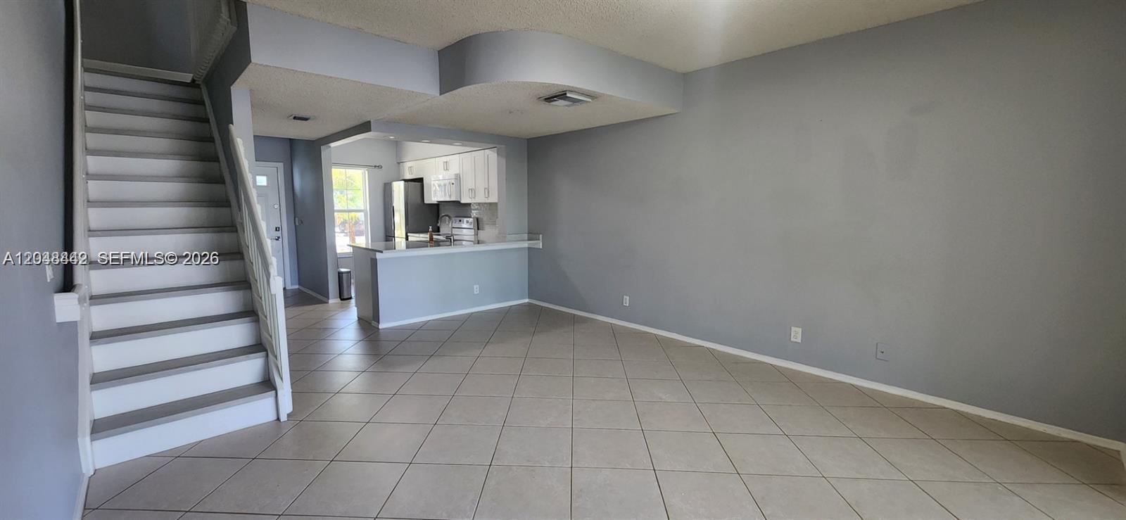 An open-concept living area features tiled floors, a staircase, and a kitchen with white cabinets — 211 Mallory Ct, Weston FL 33326, WESTON, FL