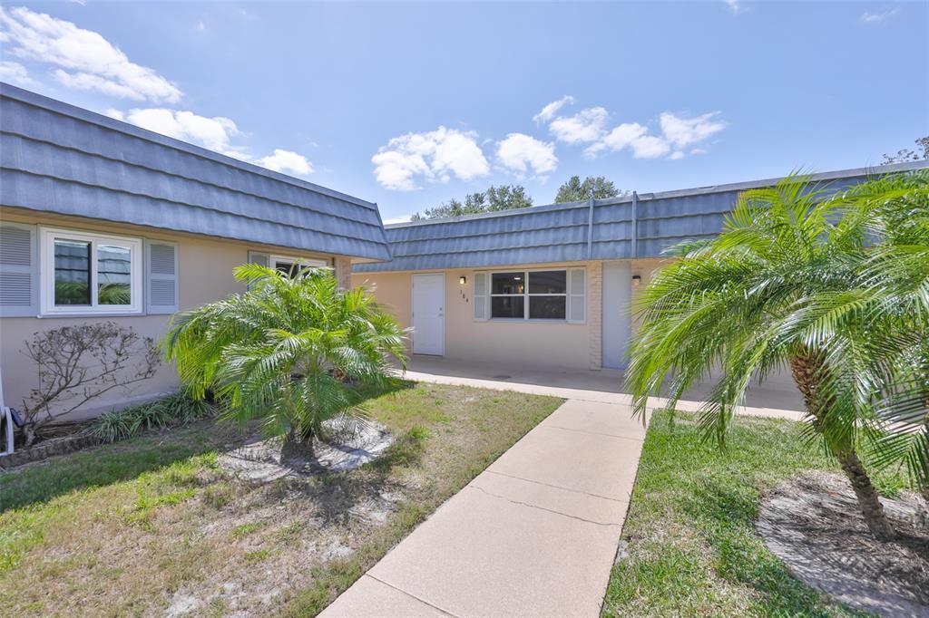 A sidewalk leads to the entrance of a single-story building with palm trees and landscaping — 1802 BEDFORD TERRACE UNIT 184, SUN CITY CENTER, FL