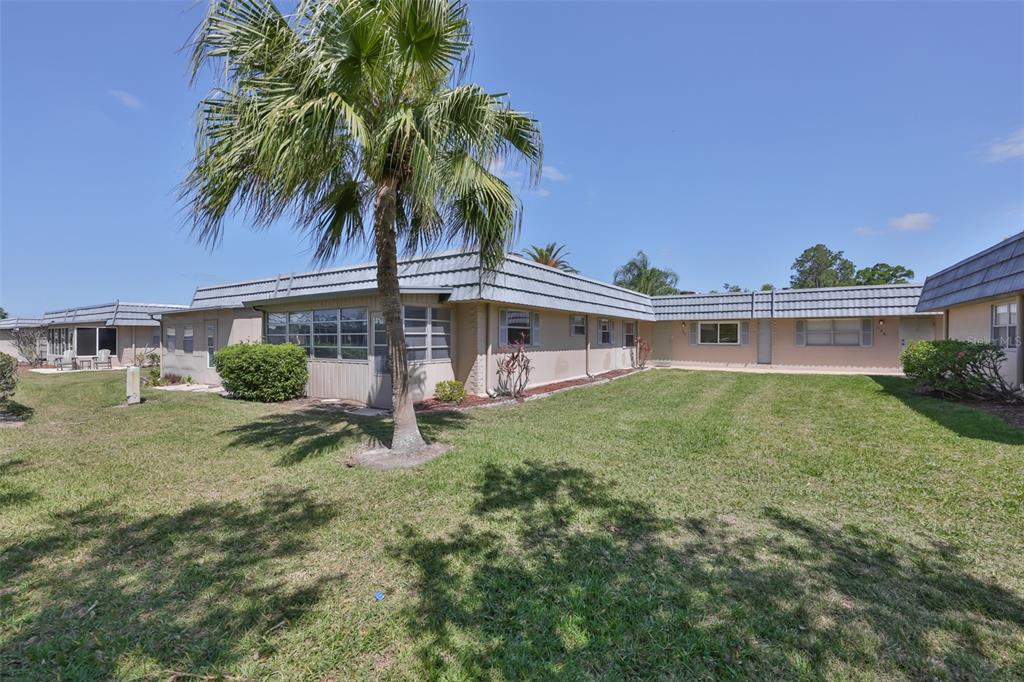 A single-story residential building with a gray tiled roof and a palm tree in front — 1802 BEDFORD TERRACE UNIT 184, SUN CITY CENTER, FL