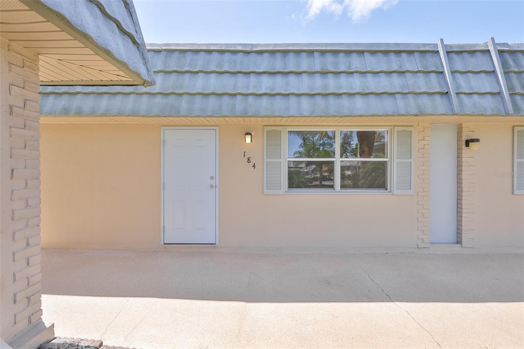 A beige exterior wall features a white door, a window with shutters, and a roofline — 1802 BEDFORD TERRACE UNIT 184, SUN CITY CENTER, FL