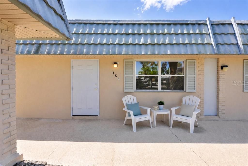 A beige exterior wall features a white door, a window with shutters, and two chairs — 1802 BEDFORD TERRACE UNIT 184, SUN CITY CENTER, FL