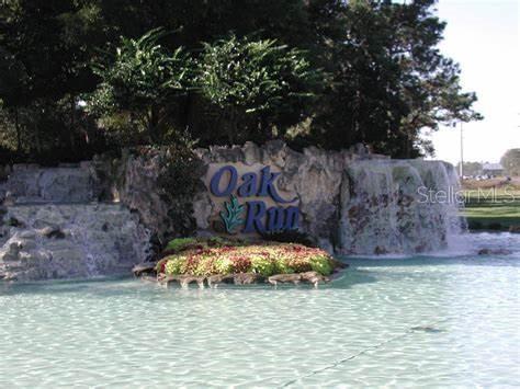 A stone waterfall feature with an Oak Run sign sits in front of a pond — 8795 SW 108TH STREET, OCALA, FL