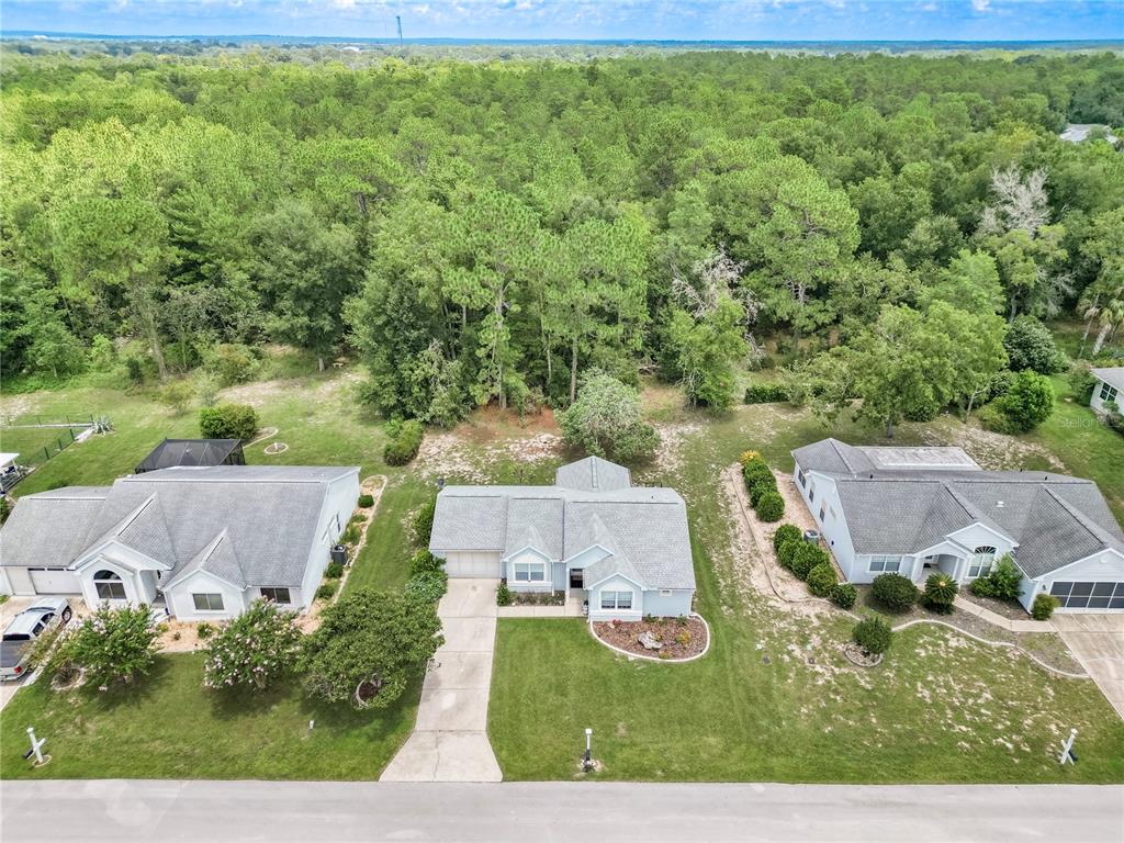 An aerial view shows three suburban houses with gray roofs and driveways bordering a forest — 8795 SW 108TH STREET, OCALA, FL