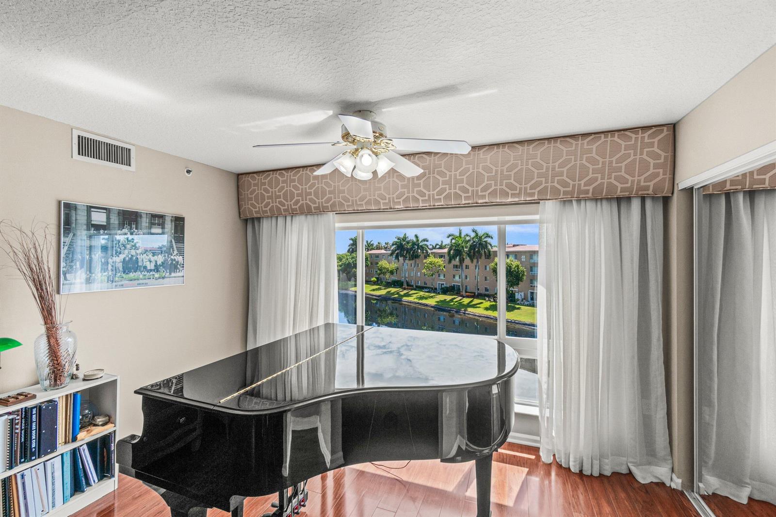 A room with a grand piano, wood flooring, and a large window overlooking a canal — 12560 Majesty Circle # 401, Boynton Beach FL 33437, BOYNTON BEACH, FL