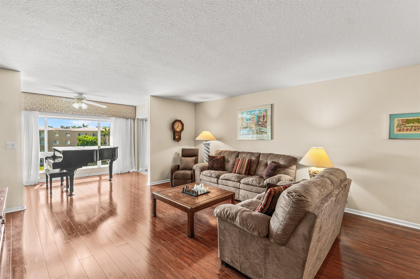 A dining area with a glass-topped rattan table sits before a living room with a piano — 12560 Majesty Circle # 401, Boynton Beach FL 33437, BOYNTON BEACH, FL