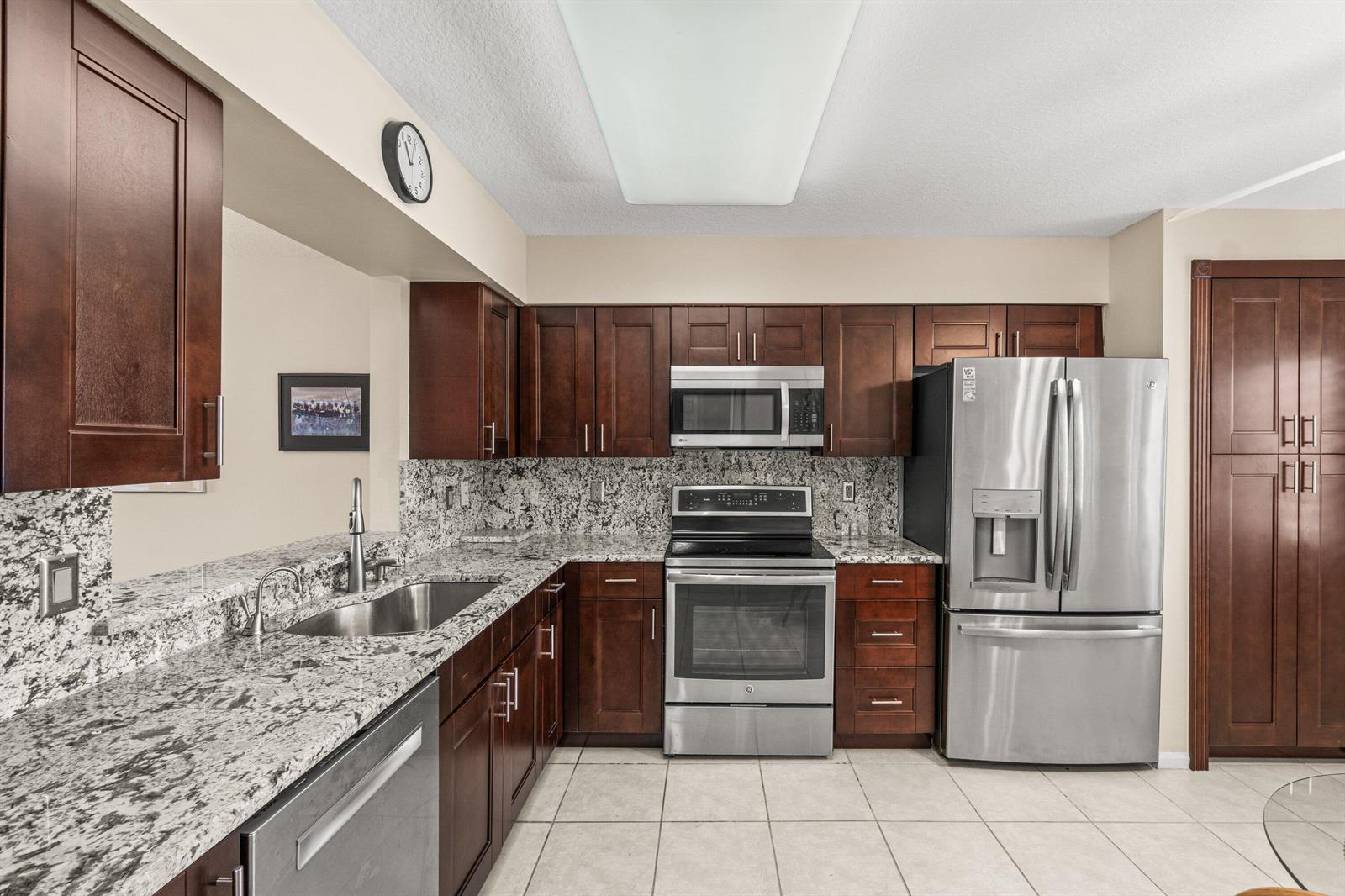 A kitchen features dark wood cabinets, granite countertops, stainless steel appliances, and tile flooring — 12560 Majesty Circle # 401, Boynton Beach FL 33437, BOYNTON BEACH, FL
