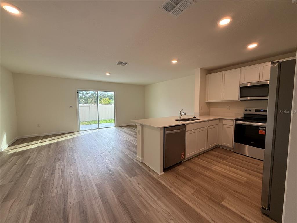An open-concept kitchen with white cabinets and stainless steel appliances overlooks a living area — 6524 SW 82ND LOOP, OCALA, FL