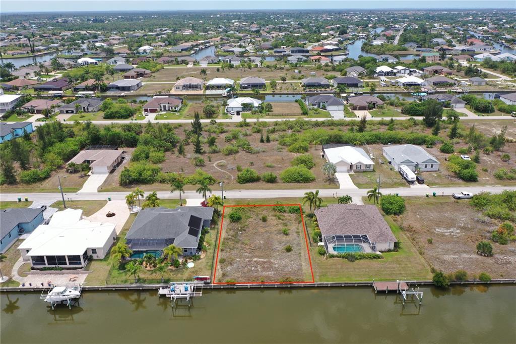 An aerial view shows a vacant waterfront lot outlined in red between two houses — 15124 TAURUS CIRCLE, PORT CHARLOTTE, FL