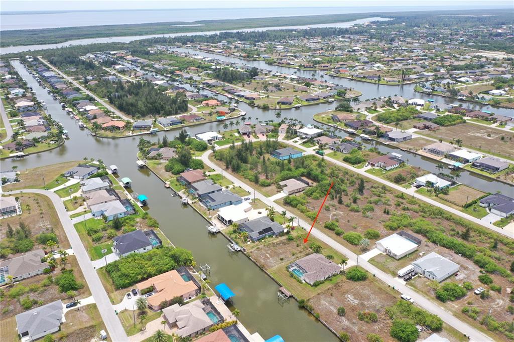 An aerial view shows a residential neighborhood with houses along canals and vacant lots — 15124 TAURUS CIRCLE, PORT CHARLOTTE, FL