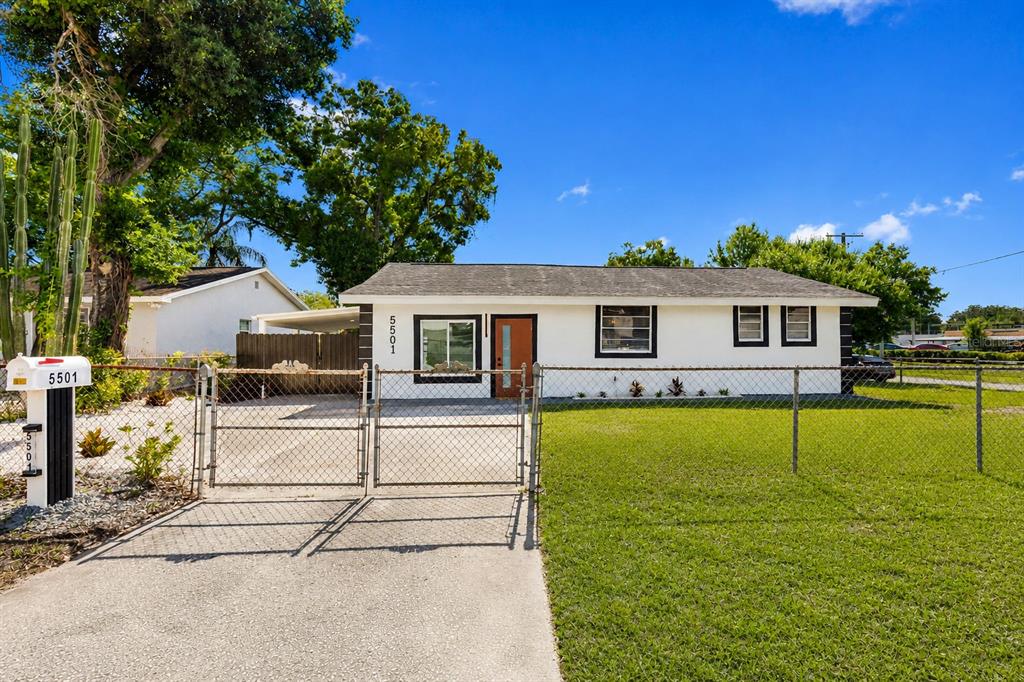 A single-story house with white siding, a brown front door, and a chain-link fence — 5501 N ALBANY AVENUE, TAMPA, FL