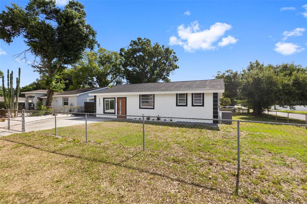 A white, single-story house with a dark roof and black trim sits behind a chain-link fence — 5501 N ALBANY AVENUE, TAMPA, FL