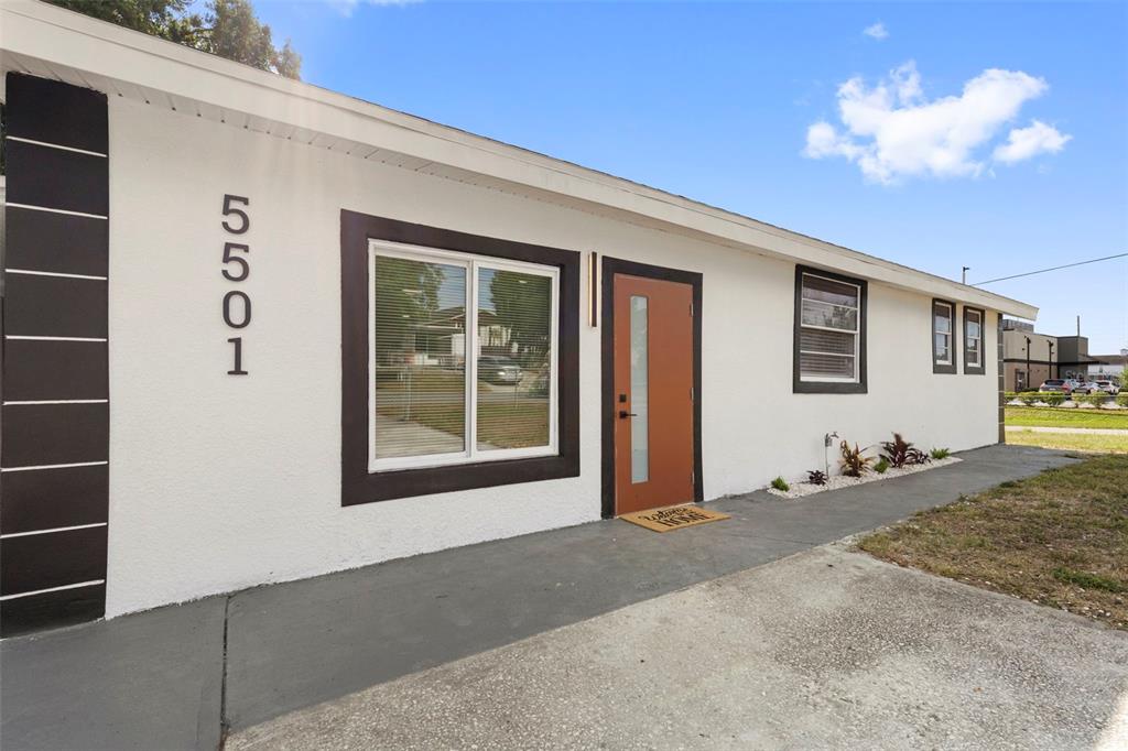 The exterior of a white house features a brown door, dark trim, and house numbers — 5501 N ALBANY AVENUE, TAMPA, FL
