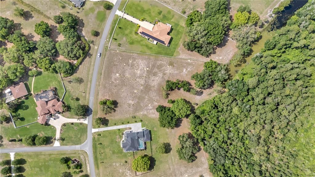 An aerial view shows a vacant residential lot situated between two houses and a wooded area — LOT 67, GRAND OAK LANE, TAVARES, FL