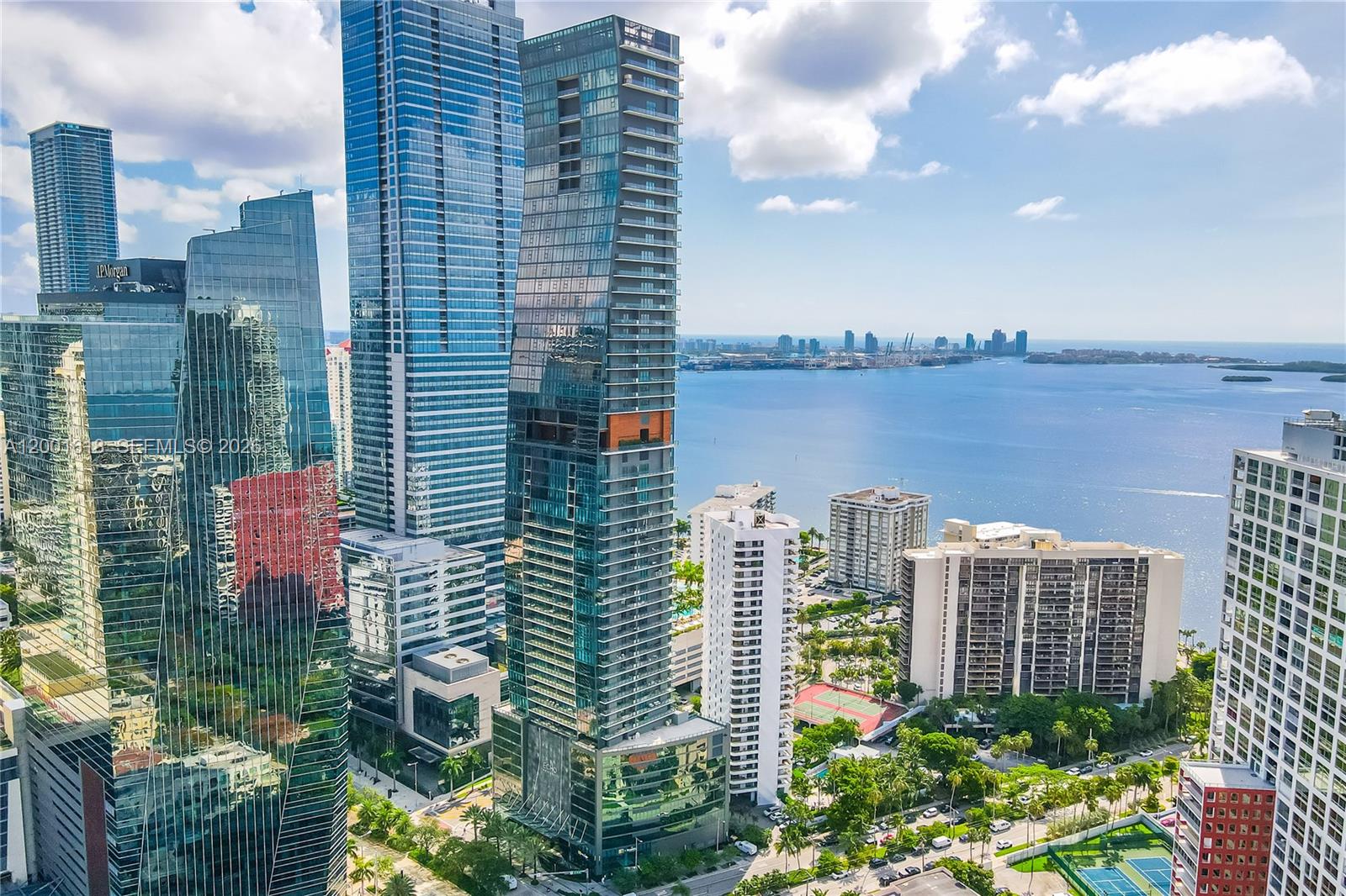 An aerial view shows several modern glass skyscrapers and residential buildings near a large bay — 1451 Brickell Ave # 1004, Miami FL 33131, MIAMI, FL