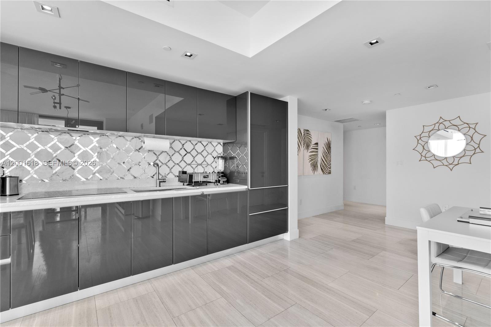 A modern kitchen features glossy gray cabinets, a mirrored backsplash, and light-colored tile flooring — 1451 Brickell Ave # 1004, Miami FL 33131, MIAMI, FL
