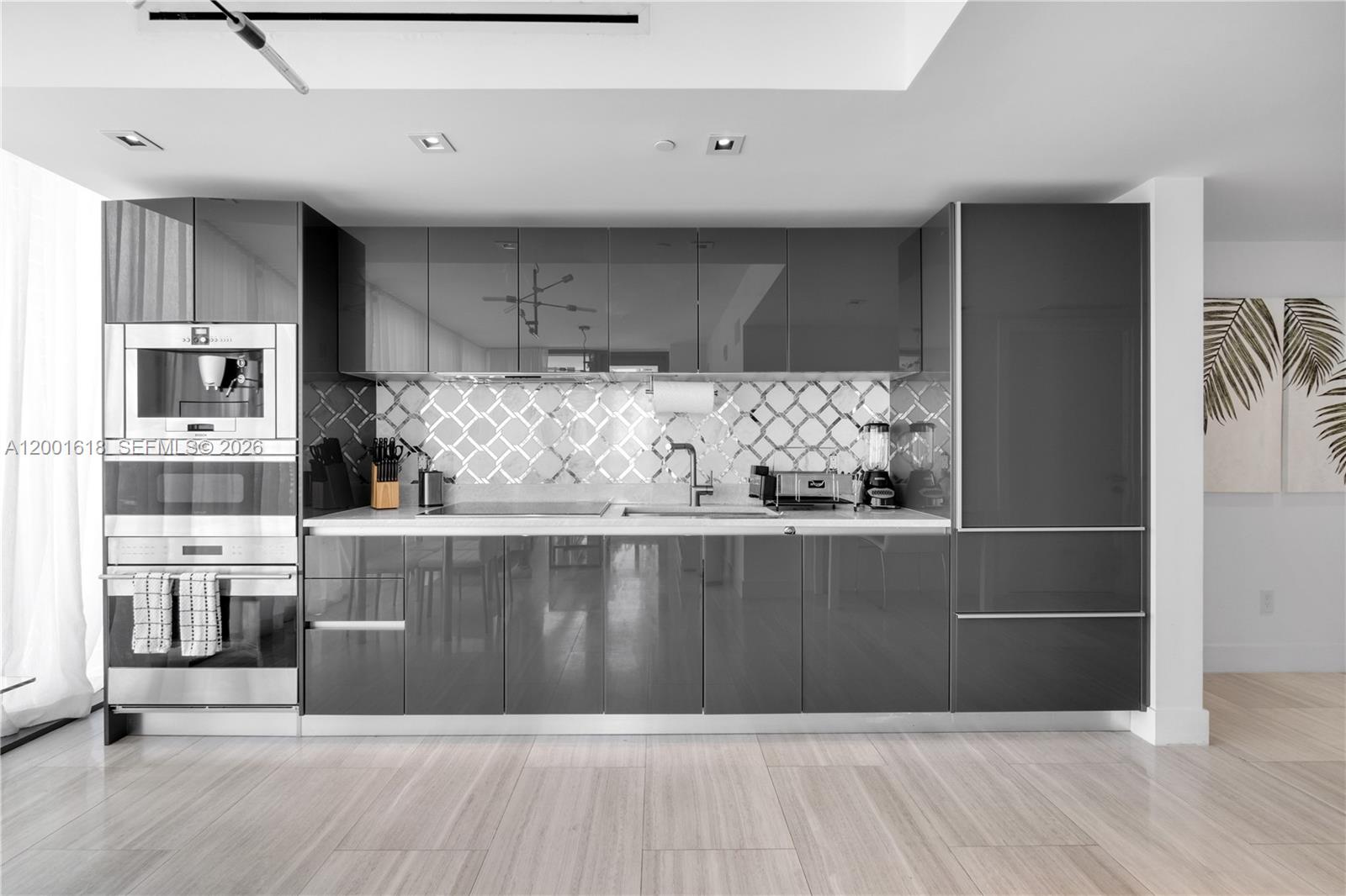 A modern kitchen features glossy gray cabinets, a mirrored backsplash, and stainless steel appliances — 1451 Brickell Ave # 1004, Miami FL 33131, MIAMI, FL