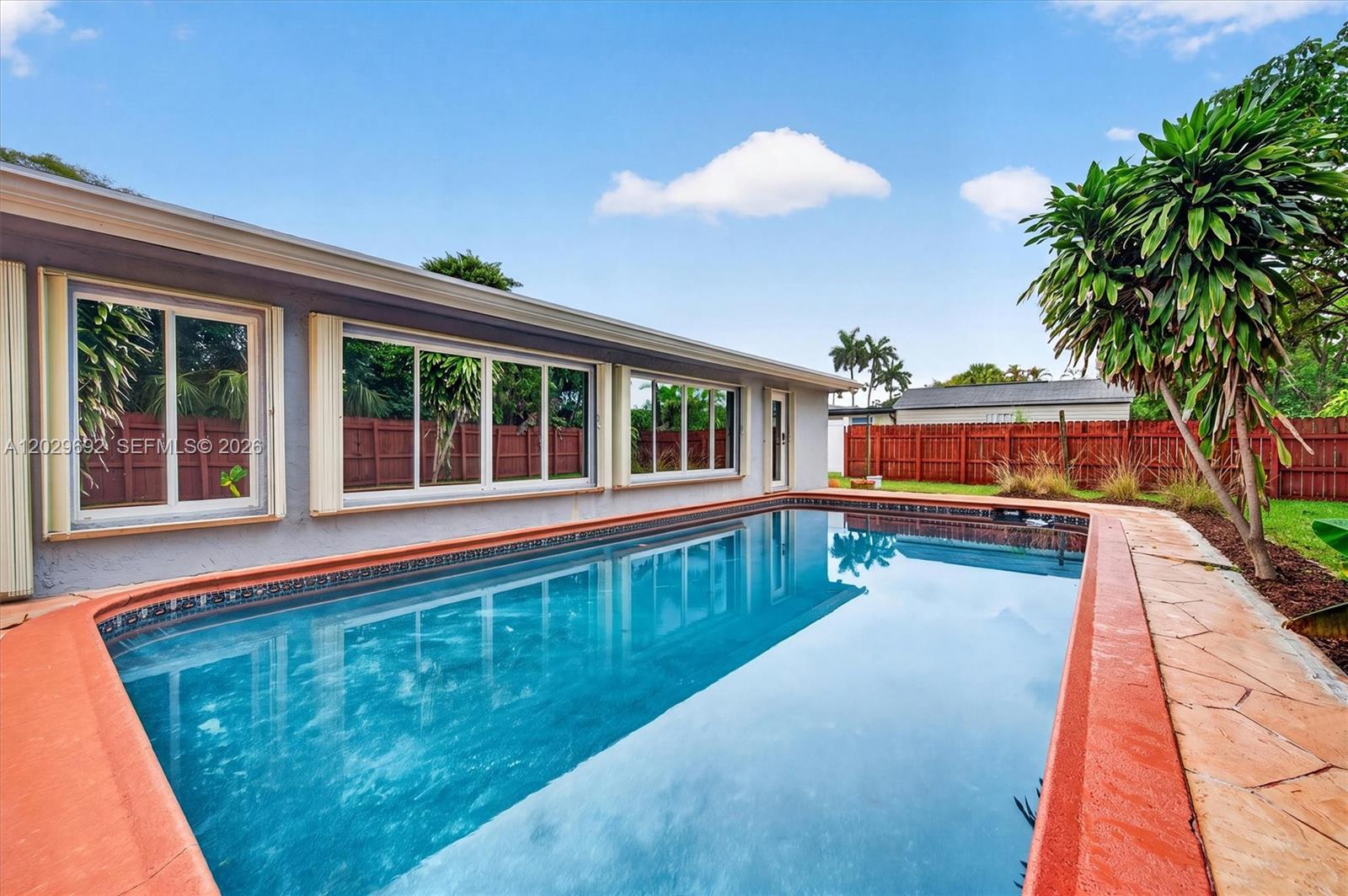 A rectangular swimming pool sits beside a house with large windows and a wooden fence — 5501 Pine Ter, Plantation FL 33317, PLANTATION, FL