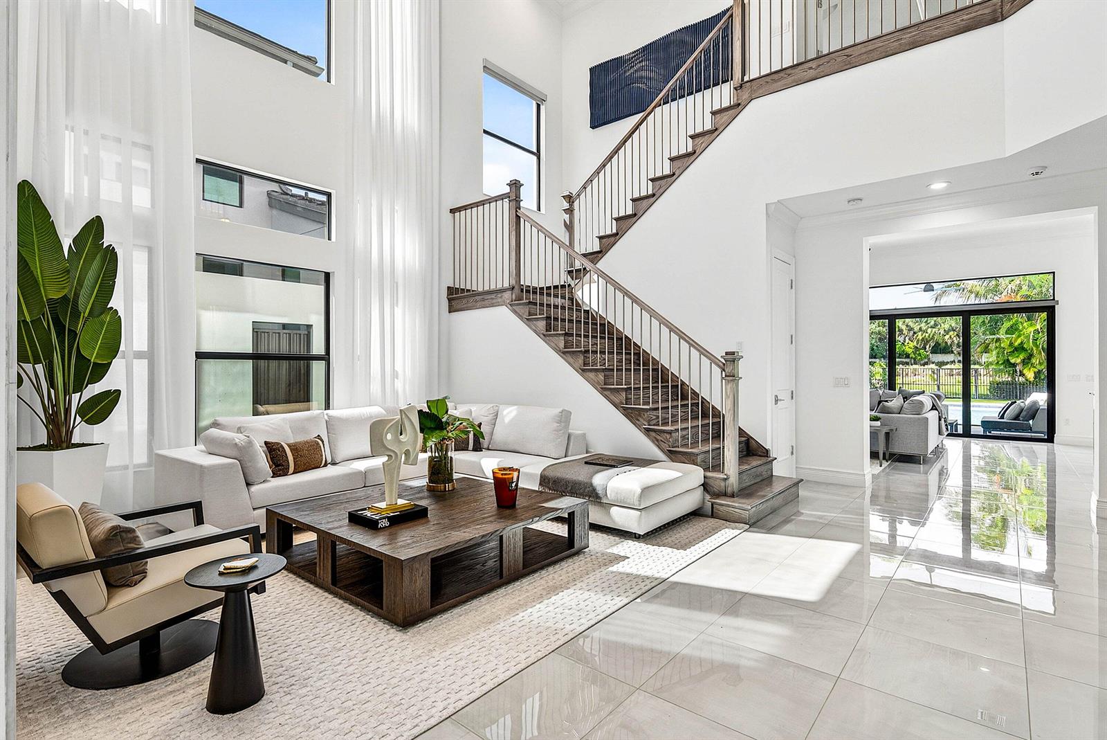 A modern living room features a wooden staircase, white sectional sofa, and large floor-to-ceiling windows — 9065 Benedetta Place, Boca Raton FL 33496, BOCA RATON, FL