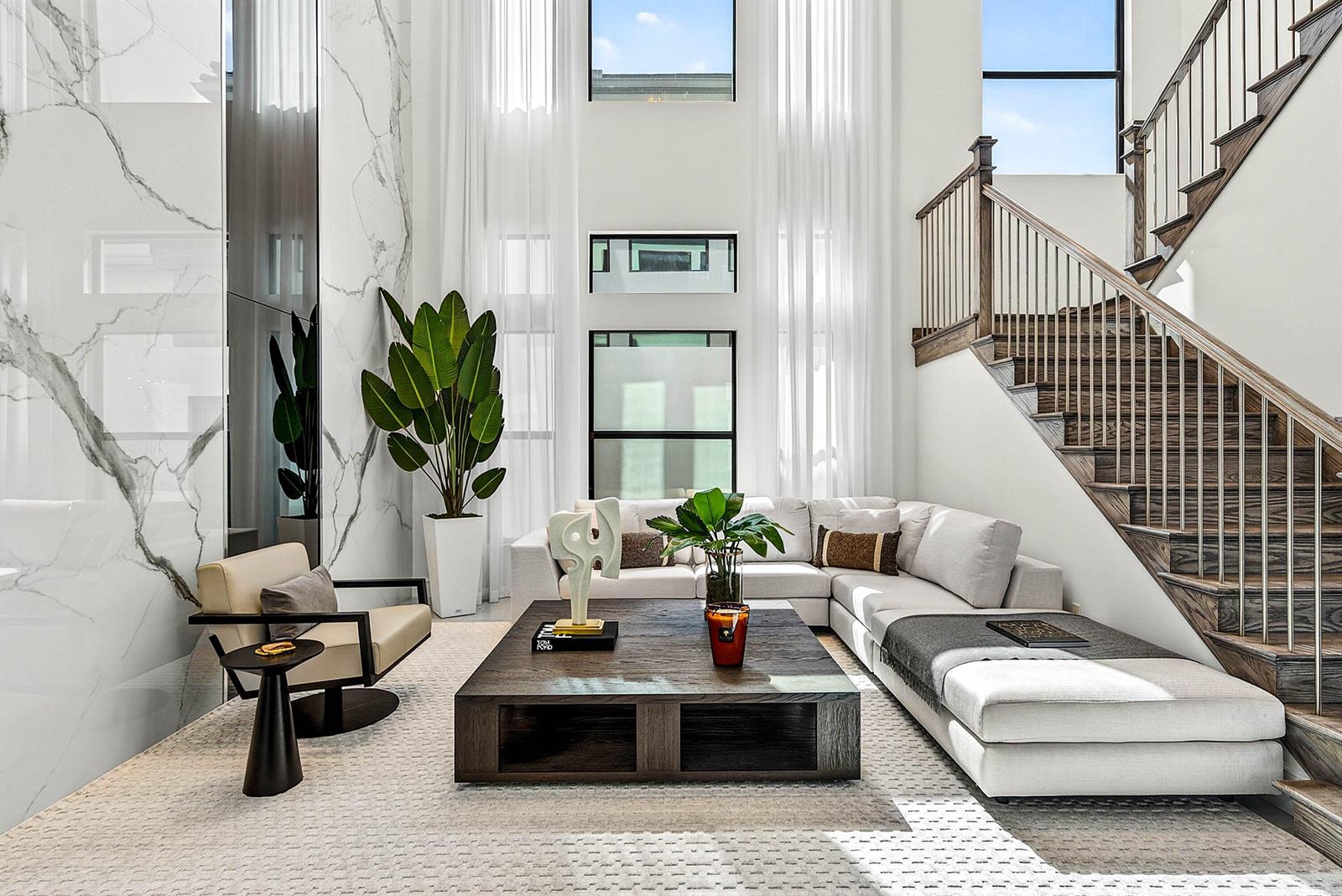 A modern living room features a double-height ceiling, marble accent wall, and wooden staircase — 9065 Benedetta Place, Boca Raton FL 33496, BOCA RATON, FL