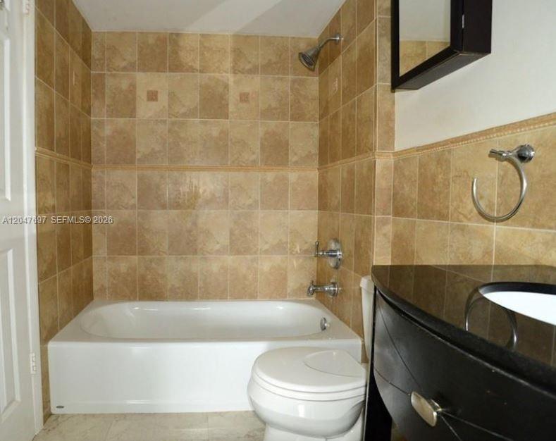 A bathroom features a white bathtub, a toilet, and a black vanity with tan tiles — 510 NW 86th # 12, Miami FL 33126, MIAMI, FL