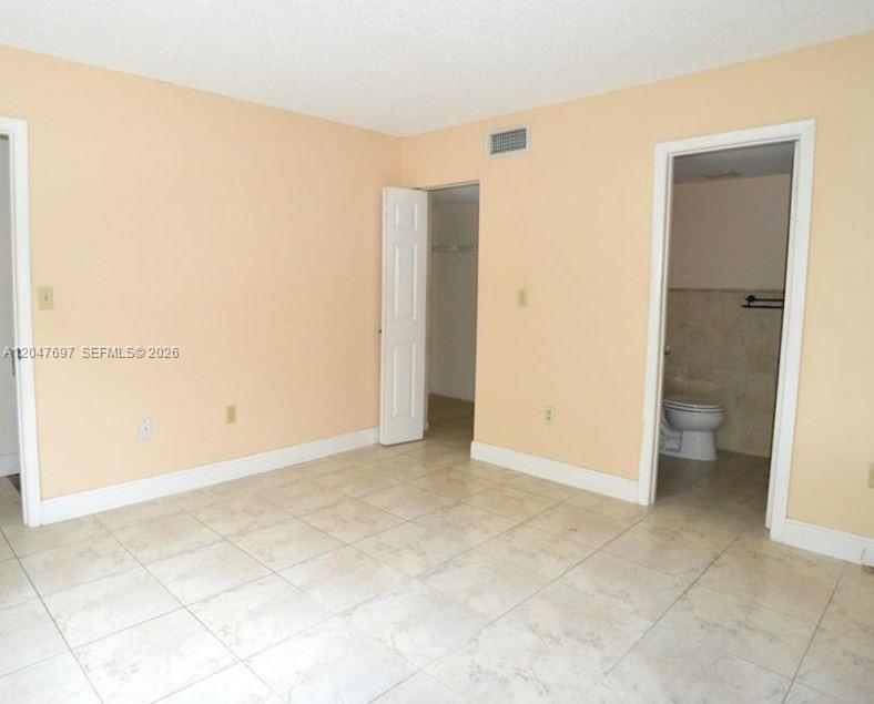 An empty room with light-colored tile flooring, peach walls, a closet, and an attached bathroom — 510 NW 86th # 12, Miami FL 33126, MIAMI, FL