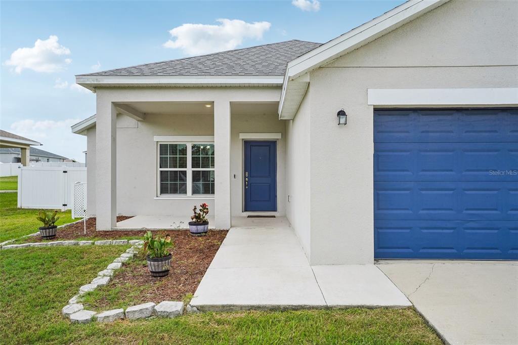 The exterior of a light-colored house features a blue front door and a blue garage — 5494 SE 91ST STREET, OCALA, FL