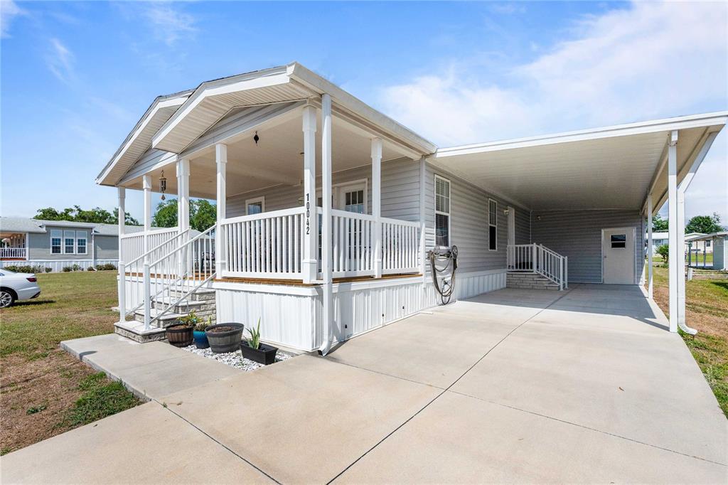 A light gray manufactured home features a front porch, a concrete driveway, and a carport — 10042 COLLINGWOOD AVENUE, DADE CITY, FL