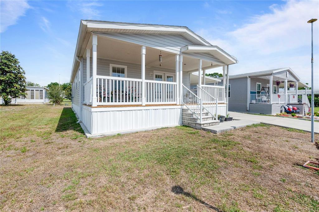 A light gray manufactured home features a covered front porch with white railings and stairs — 10042 COLLINGWOOD AVENUE, DADE CITY, FL