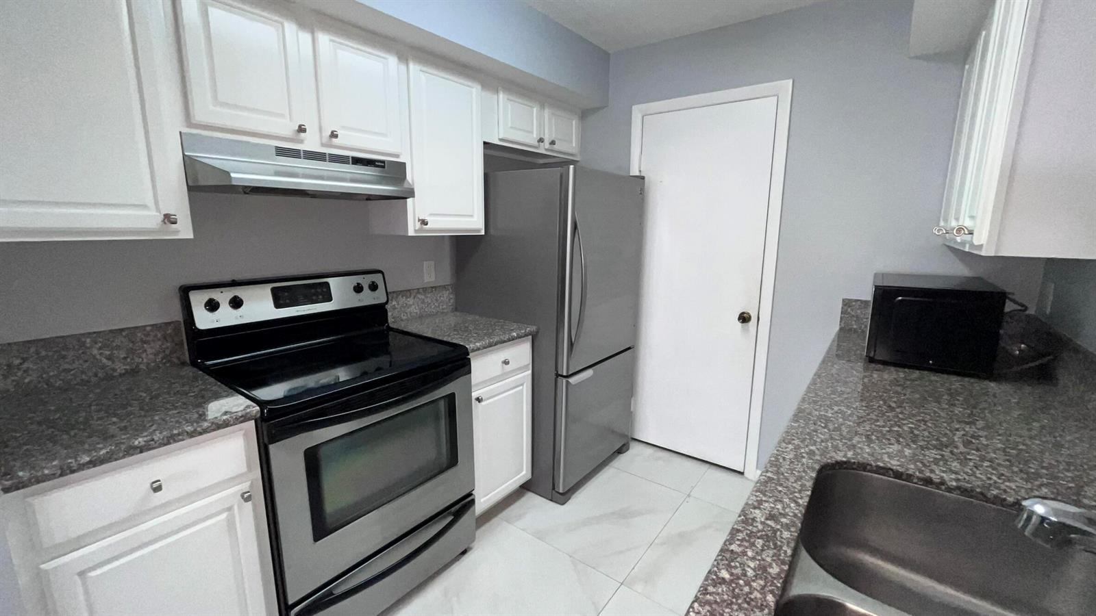 A kitchen features white cabinets, granite countertops, stainless steel appliances, and light-colored tile flooring — 815 W Boynton Beach Boulevard # 107, Boynton Beach FL 33426, BOYNTON BEACH, FL
