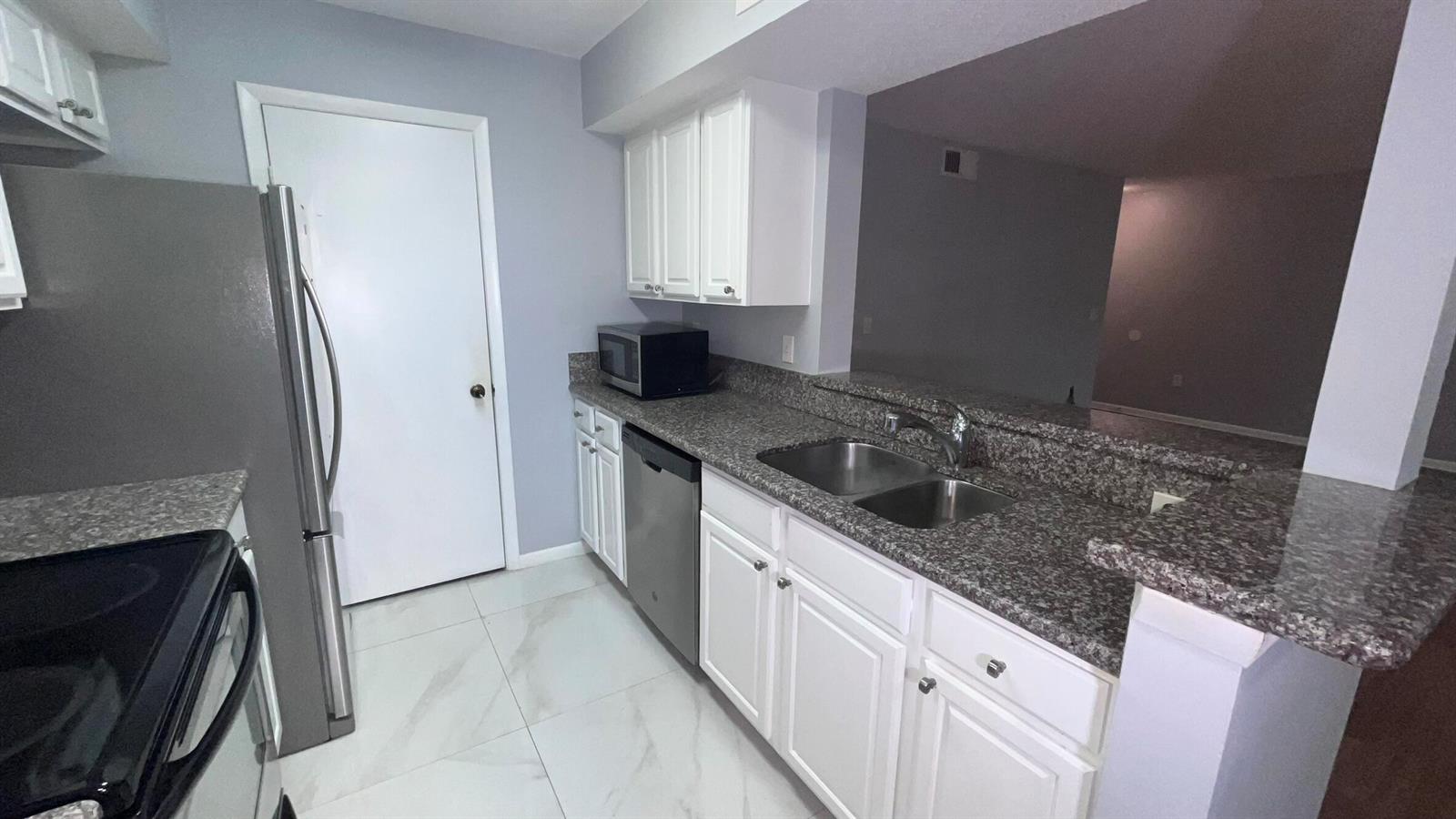A kitchen features white cabinets, granite countertops, stainless steel appliances, and light-colored tile flooring — 815 W Boynton Beach Boulevard # 107, Boynton Beach FL 33426, BOYNTON BEACH, FL