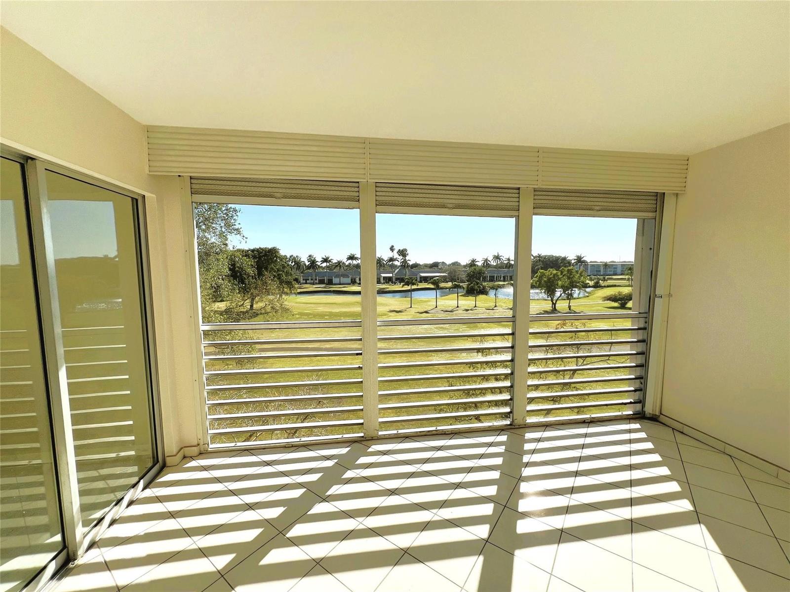 A sunroom with white tile floors and louvered windows overlooking a golf course and pond — 3303 Aruba Way # 4, Coconut Creek FL 33066, COCONUT CREEK, FL