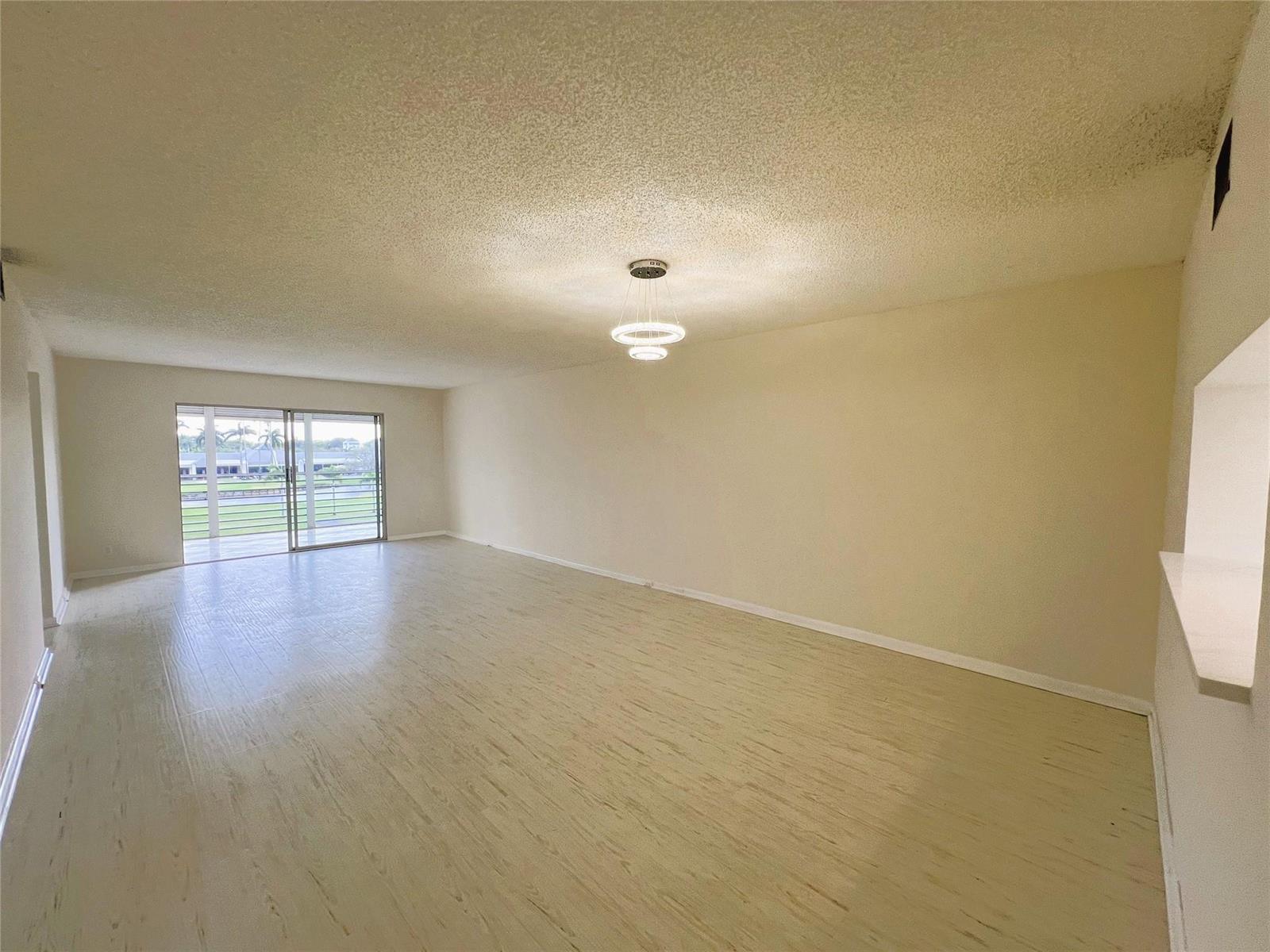 An empty living room with light wood-look flooring, a modern light fixture, and sliding doors — 3303 Aruba Way # 4, Coconut Creek FL 33066, COCONUT CREEK, FL