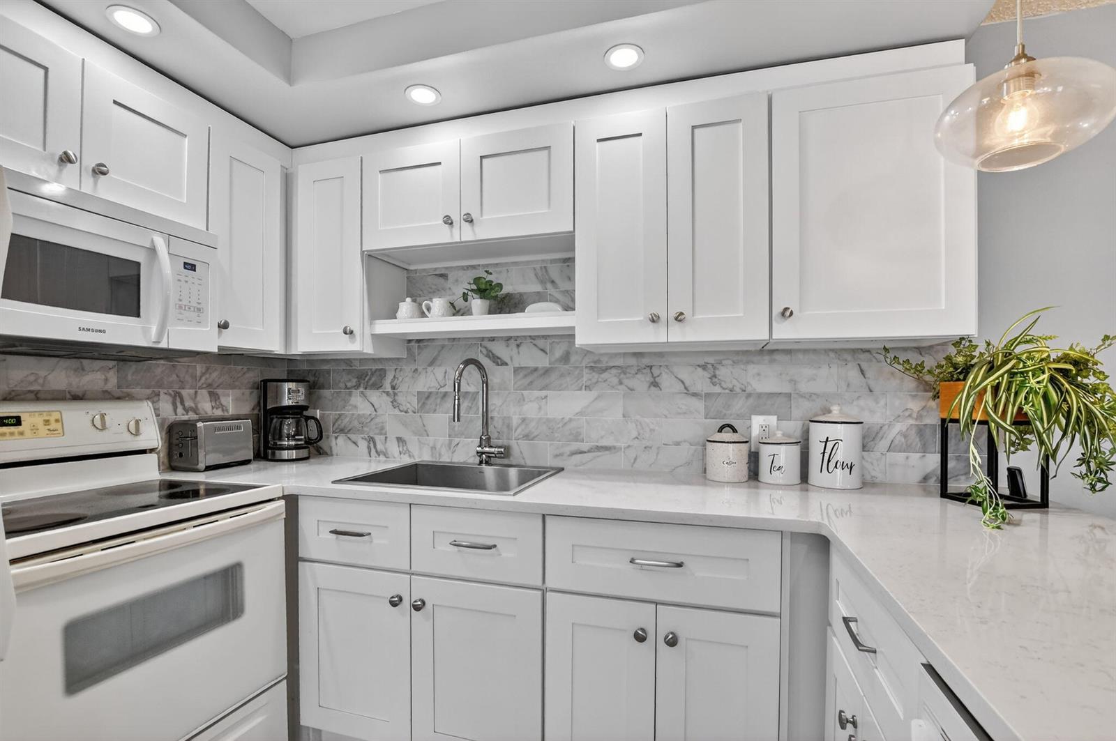 A white kitchen features marble tile backsplash, quartz countertops, and stainless steel appliances — 2074 Cambridge D, Deerfield Beach FL 33442, DEERFIELD BEACH, FL