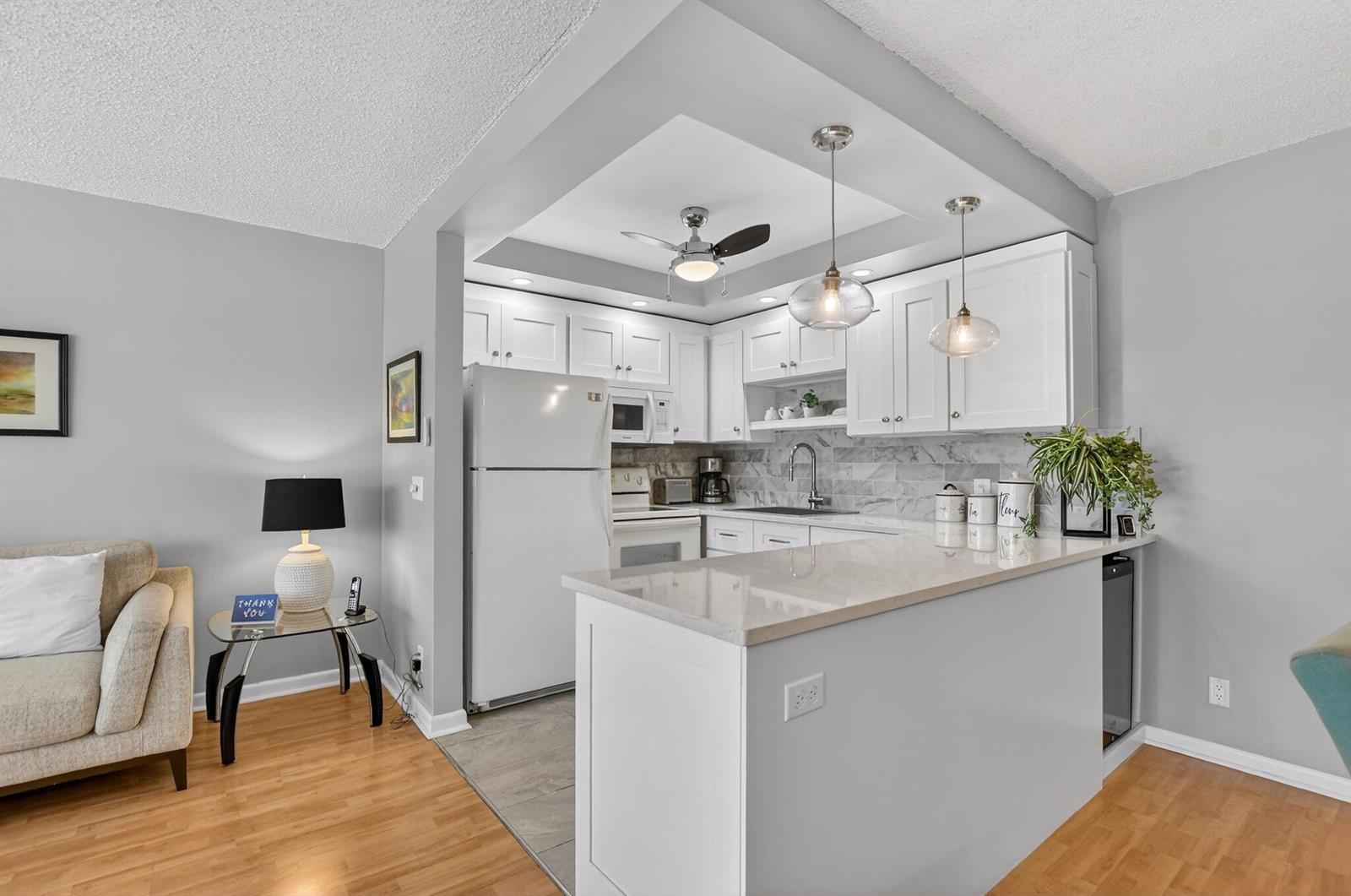 A kitchen with white cabinets, stone countertops, and a breakfast bar opens to a living area — 2074 Cambridge D, Deerfield Beach FL 33442, DEERFIELD BEACH, FL