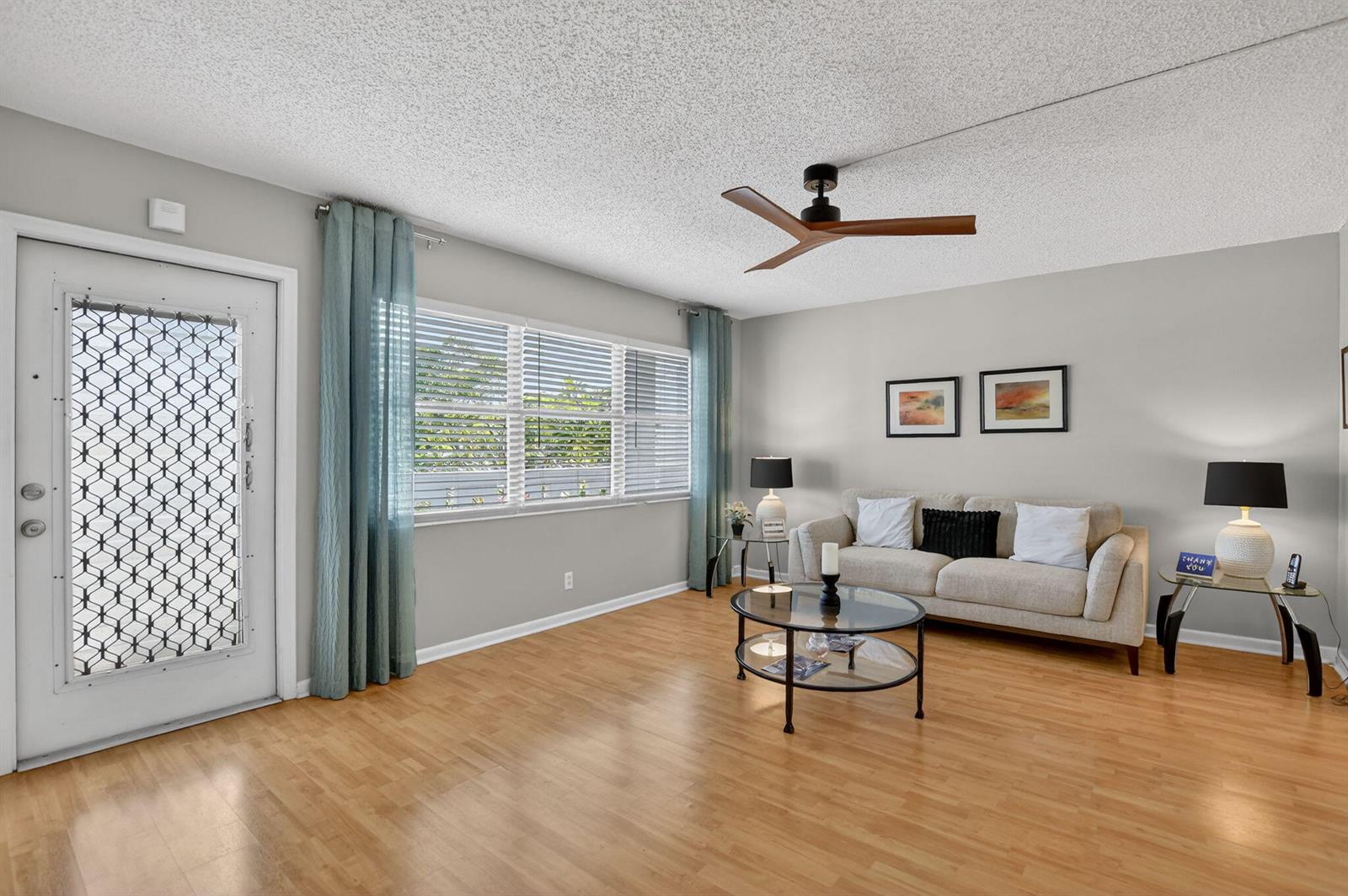 A living room features light wood flooring, a beige sofa, and a modern ceiling fan — 2074 Cambridge D, Deerfield Beach FL 33442, DEERFIELD BEACH, FL