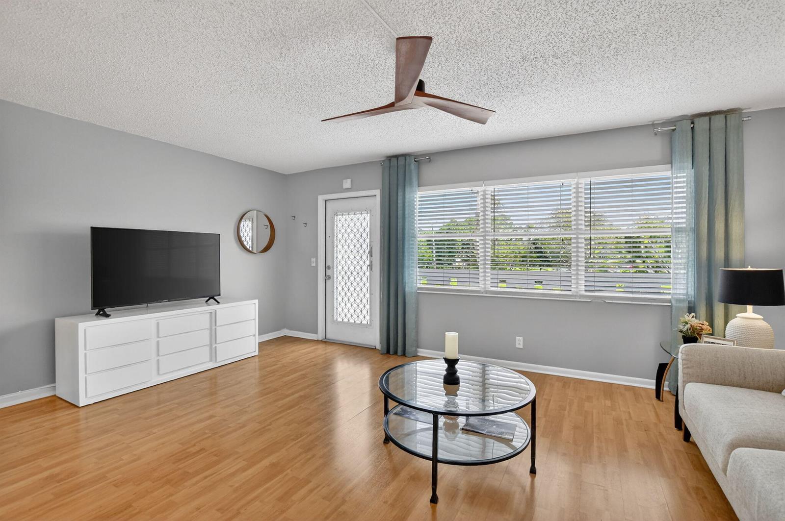 A living room features light wood floors, a white media console, and a ceiling fan — 2074 Cambridge D, Deerfield Beach FL 33442, DEERFIELD BEACH, FL