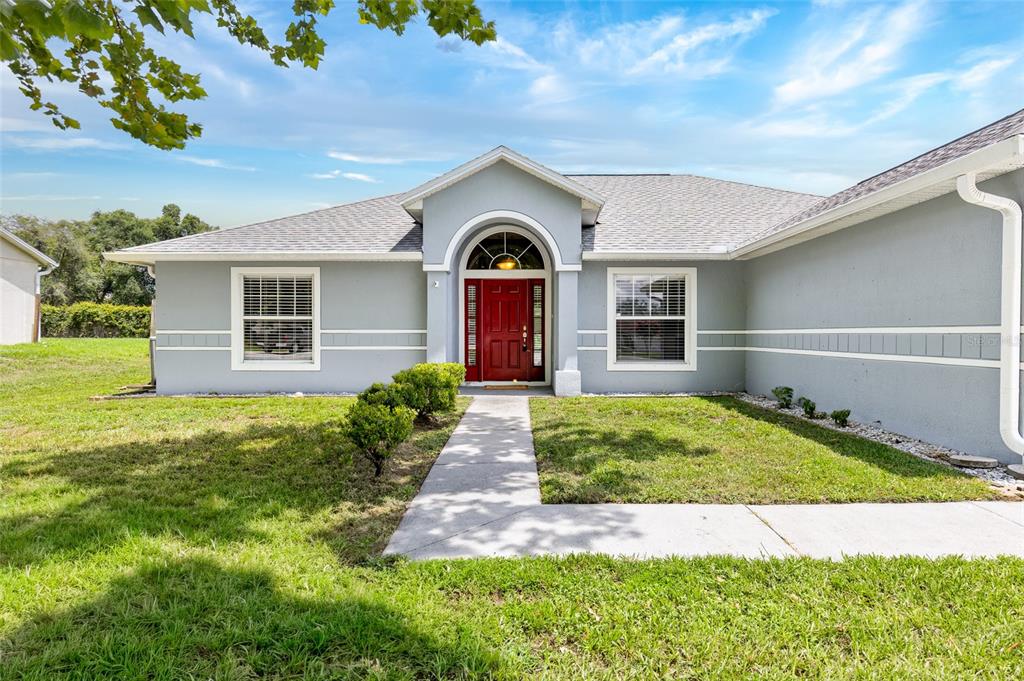 A single-story gray house with a red front door and a concrete walkway — 148 COUNTRY LAKES CIRCLE, GROVELAND, FL
