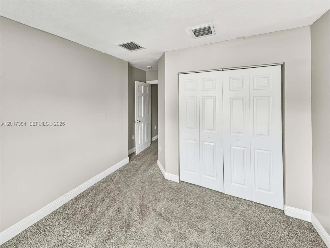 A bedroom with gray carpet, light-colored walls, and white closet doors — DAVIE, FL
