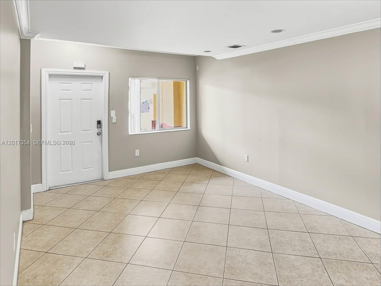 An empty room features beige walls, white trim, and light-colored diagonal floor tiles — DAVIE, FL