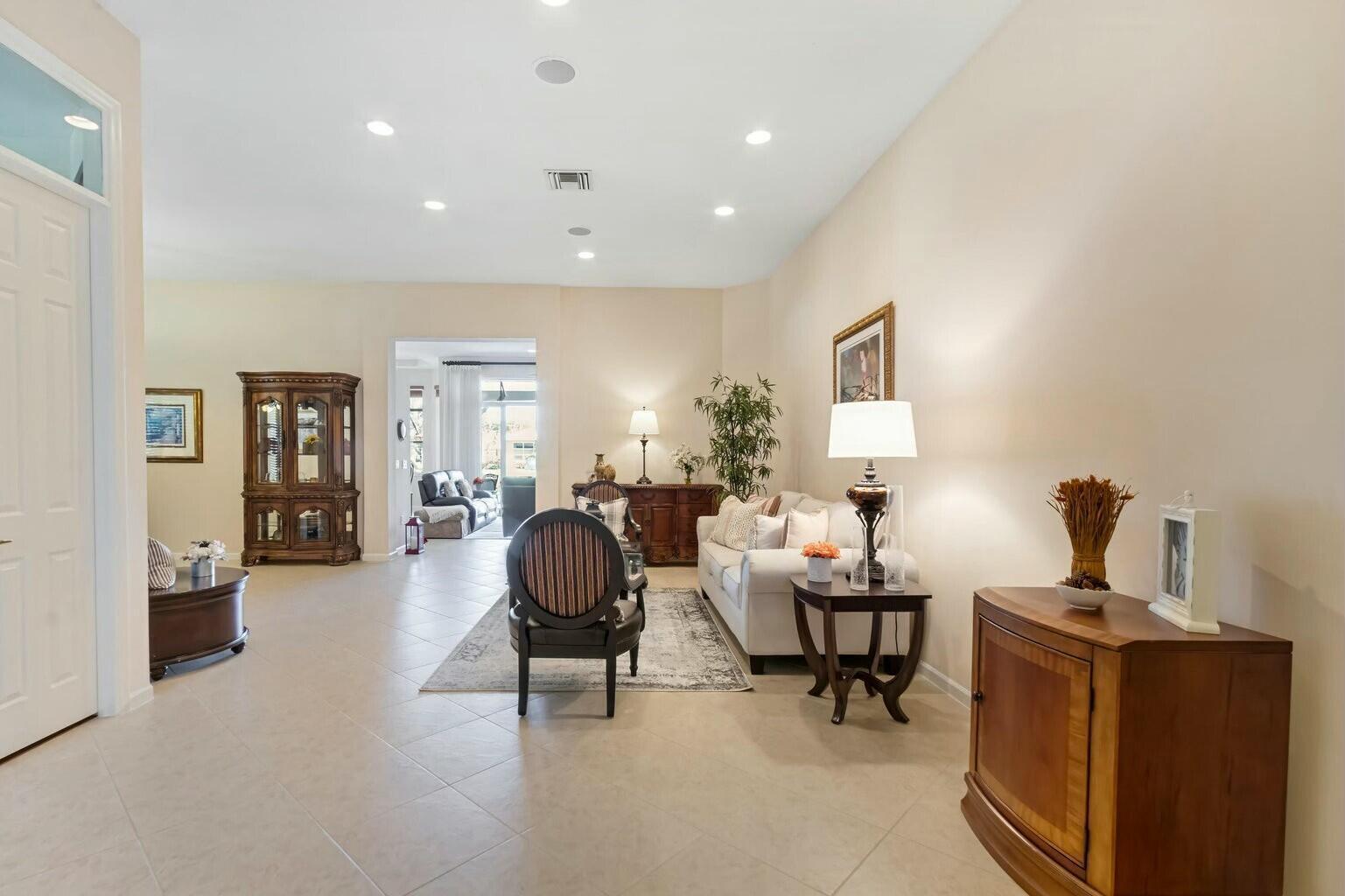 A living room features tile flooring, a beige sofa, a dark wood cabinet, and recessed lighting — 8709 Via Grande E, Wellington FL 33411, WELLINGTON, FL