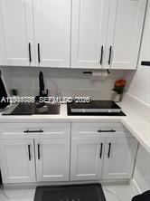 A small kitchen area features white cabinets, a black faucet, and a black cooktop — 1130 NE 201st Ter # B, Miami FL 33179, MIAMI, FL