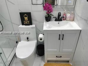 A modern bathroom features a white vanity, a toilet, and white marble-style wall tiles — 1130 NE 201st Ter # B, Miami FL 33179, MIAMI, FL