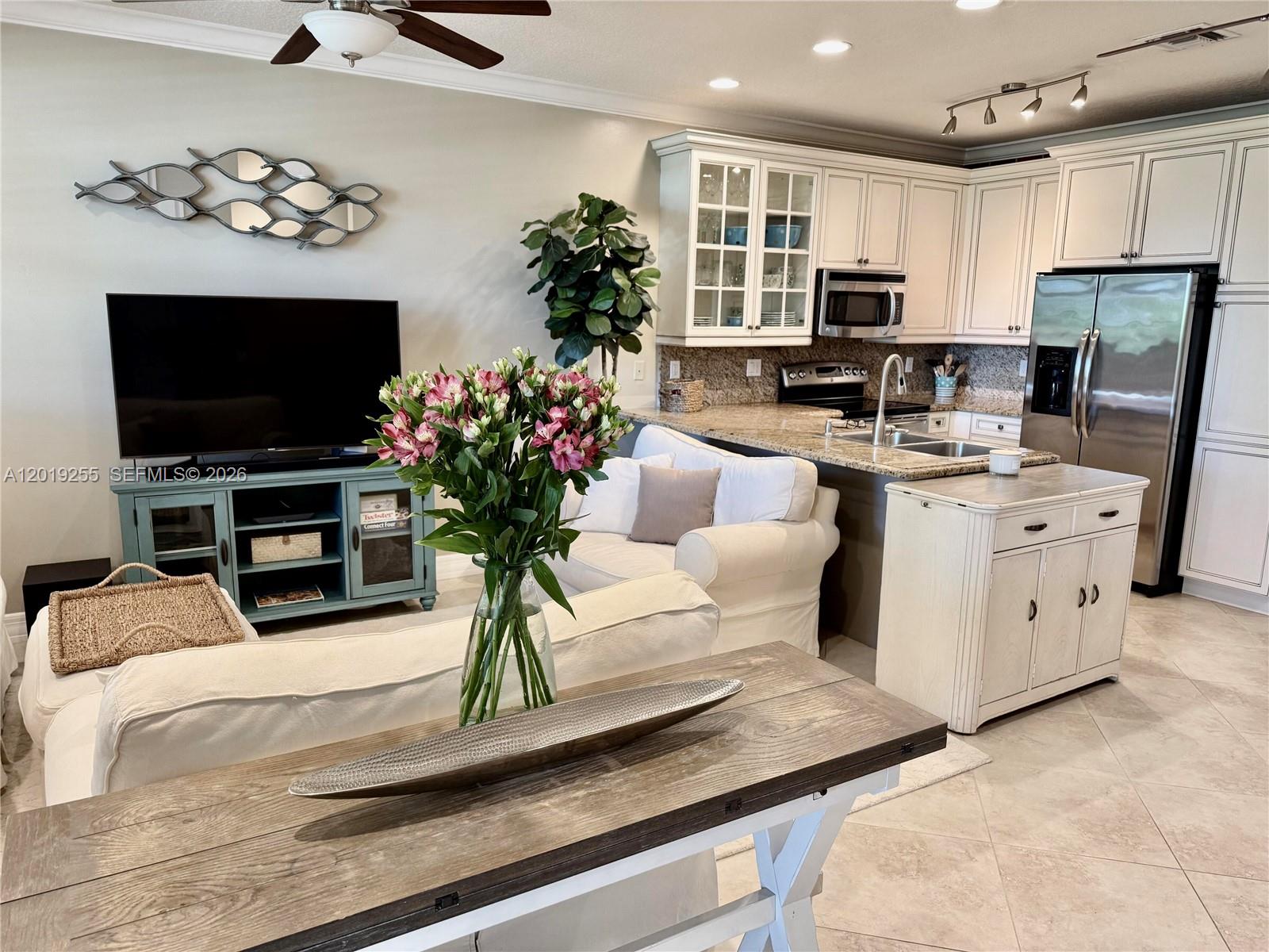 An open-concept living room and kitchen feature white cabinetry, stainless steel appliances, and tile flooring — 867 S Ocean Blvd, Pompano Beach FL 33062, POMPANO BEACH, FL