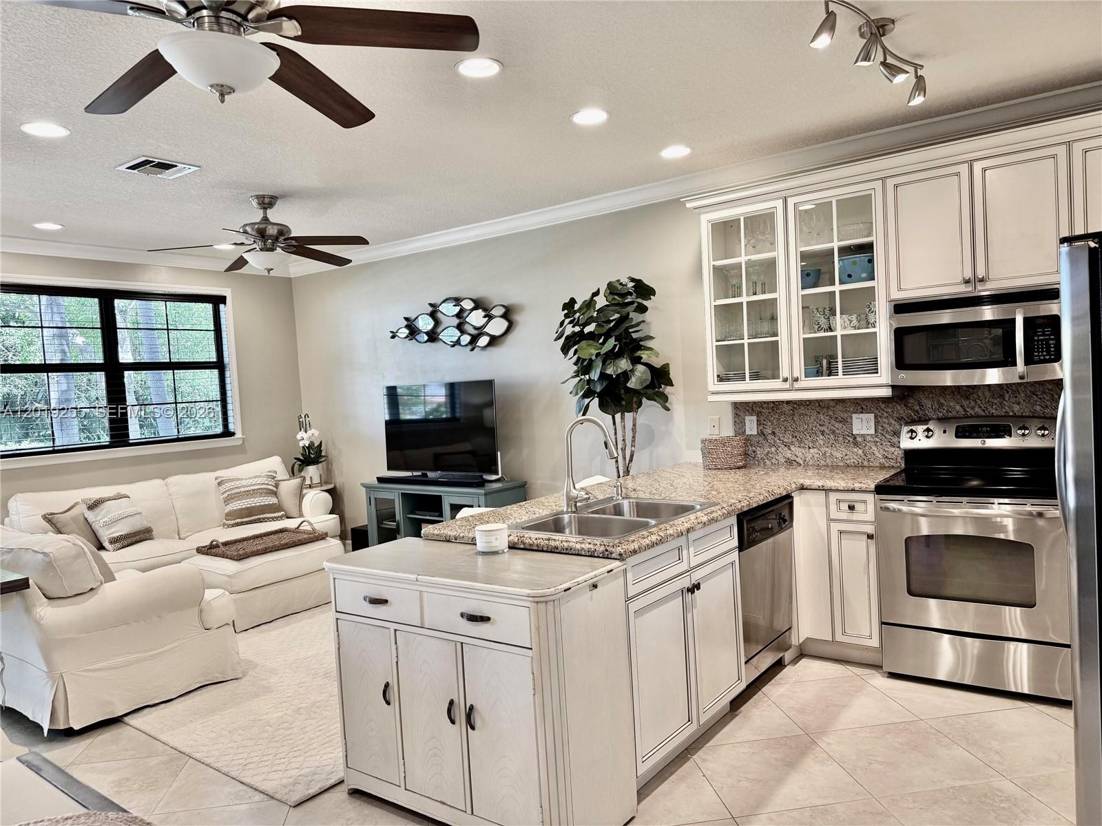 An open-concept kitchen and living area features white cabinetry, granite countertops, and stainless appliances — 867 S Ocean Blvd, Pompano Beach FL 33062, POMPANO BEACH, FL