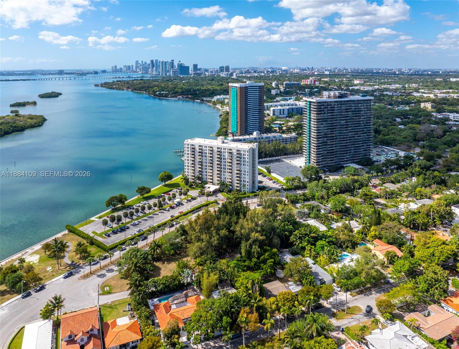 An aerial view shows high-rise apartment buildings situated along a waterfront with a city skyline — 891 NE 70th St, Miami FL 33138, MIAMI, FL