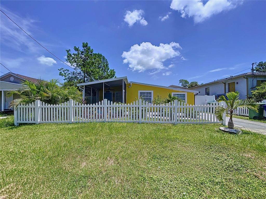 A yellow house with a white picket fence stands behind a grassy front yard — 7110 S MASCOTTE STREET, TAMPA, FL