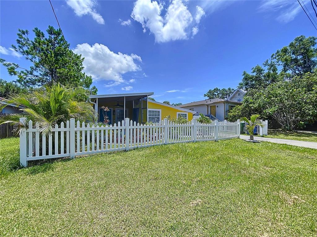 A yellow house with a white picket fence stands behind a grassy front yard — 7110 S MASCOTTE STREET, TAMPA, FL
