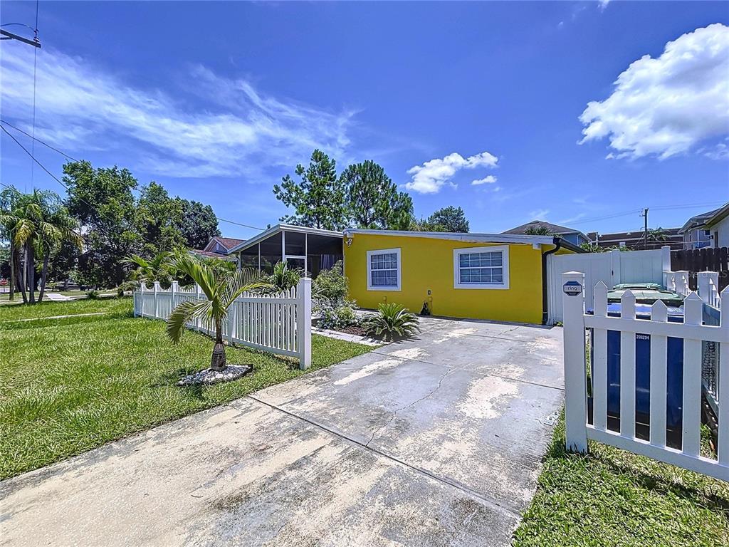 A yellow house with a white fence and a concrete driveway under a blue sky — 7110 S MASCOTTE STREET, TAMPA, FL