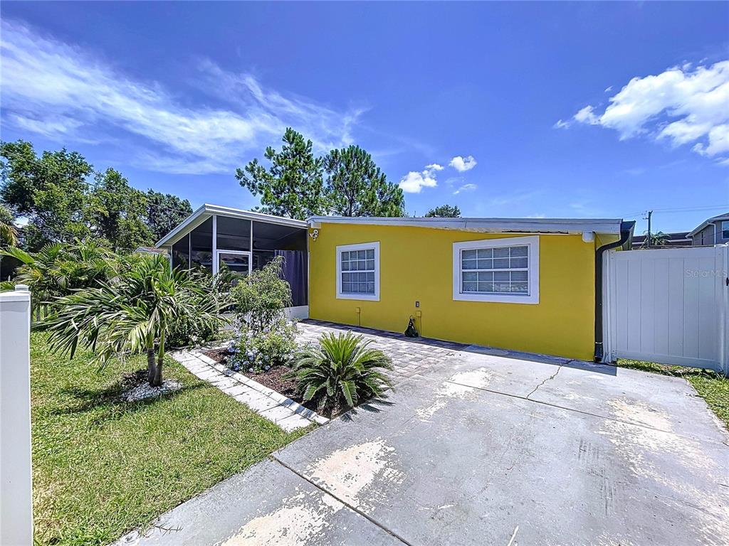 A yellow house exterior features a paved driveway, a screened porch, and a white fence — 7110 S MASCOTTE STREET, TAMPA, FL