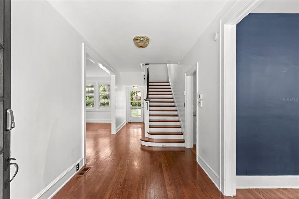A bright entryway features hardwood floors, a central staircase, and a doorway to another room — 418 JASMINE WAY, CLEARWATER, FL